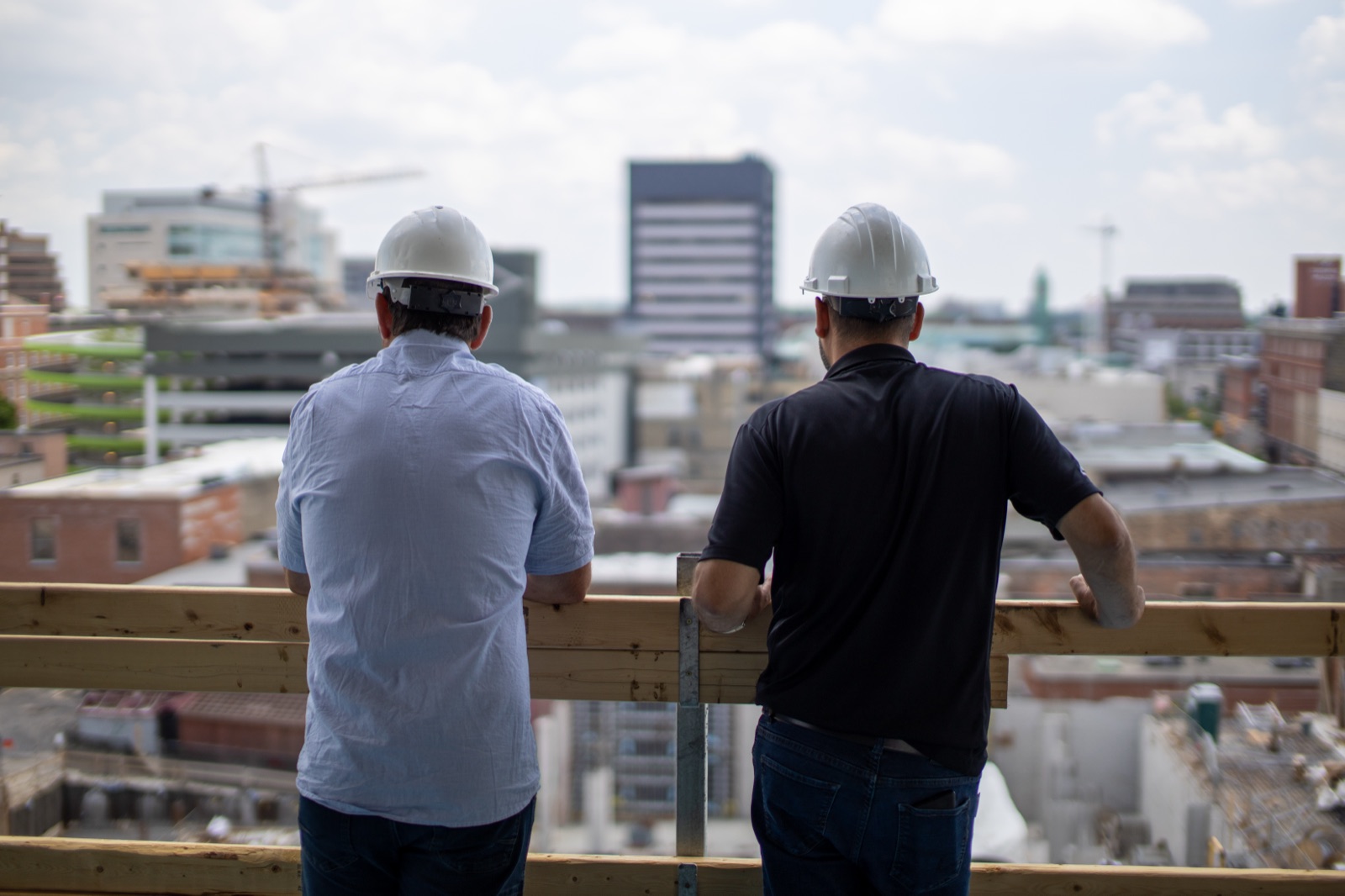 Two Jackman team members in hard hats looking out over a city skyline from a building under construction